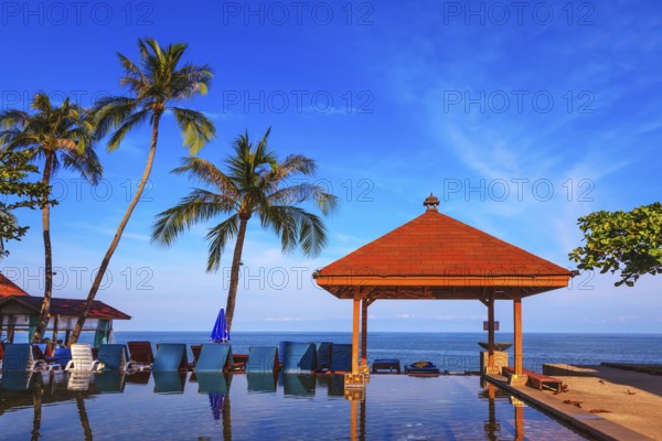 Rest of the Andaman Sea. Popular resort on the island of Koh Samui. Pool surrounded by palm trees on the sea beach. On the edge of the pool red sun canopy