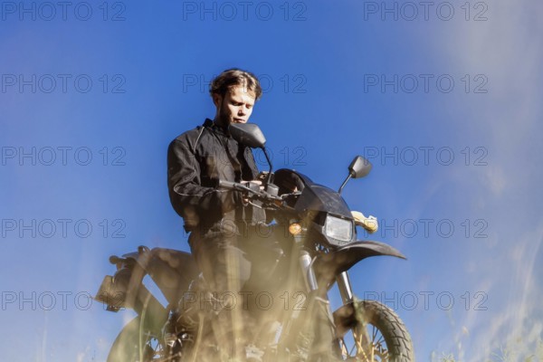 A young man in black clothing sitting on a motorcycle under a clear blue sky