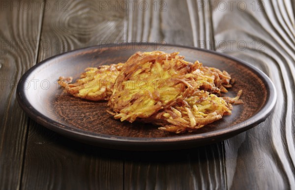 Fresh homemade tasty potato pancakes in clay dish on rustic wooden table