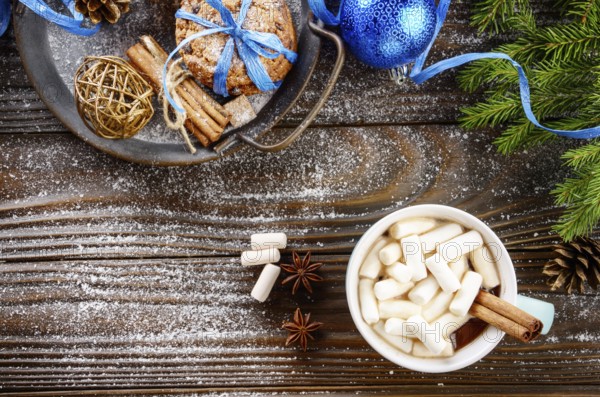 Flat lay Christmas background of blue mug with hot chocolate and marshmallows, spruce branch and tray with gingerbread cookies on wooden table