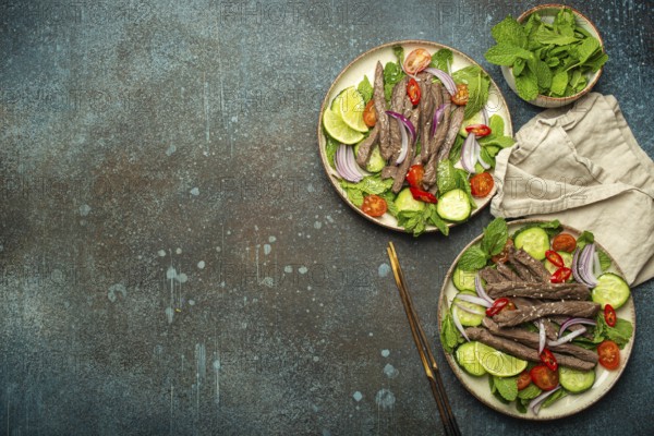 Two plates with traditional Thai beef salad with vegetables and mint top view served on rustic concrete background, healthy exotic asian meal, space for text