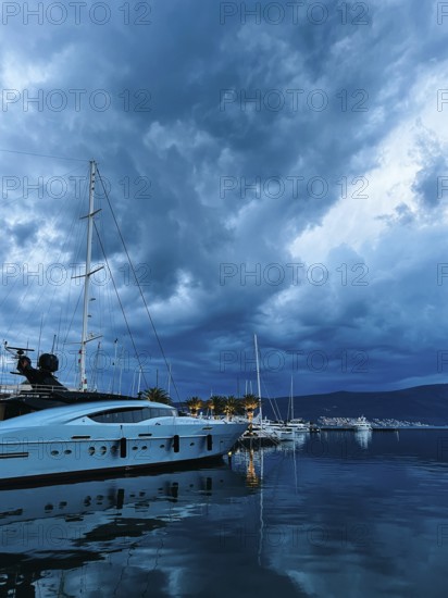 White motor yacht stands on the pier against the background of a twilight dark sky.