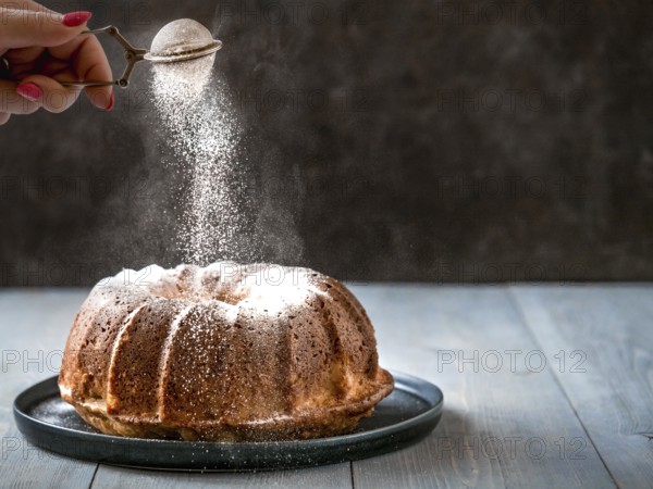 Woman's hand sprinkling icing sugar over fresh muffin cake. Powder sugar falls on fresh perfect muffin cake. Copy space for text. Ideas and recipes for breakfast or dessert