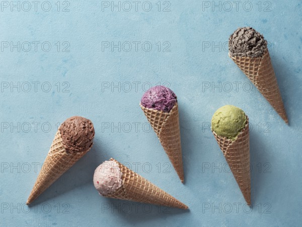 Various ice cream scoops in cones with copy space. Colorful ice cream in cones chocolate, strawberry, blueberry, pistachio or matcha, biscuits chocolate sandwich cookies on blue background. Top view