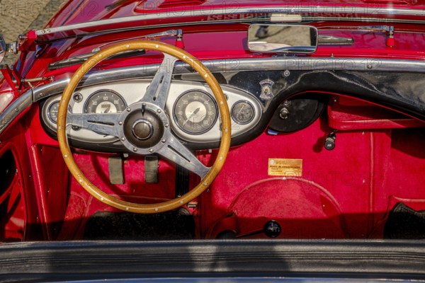 Lisbon, Portugal, Jan 20, 2024: All-red interior of Austin-Healey 100 vintage convertible sports car parked on cobblestone pavement road. Red velvet and leather, wooden steering wheel, fold-down windshield, Europe