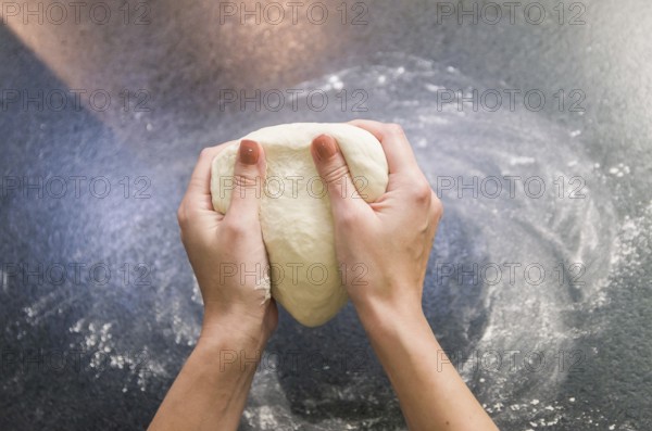 Woman preparing pizza dough on black granite table