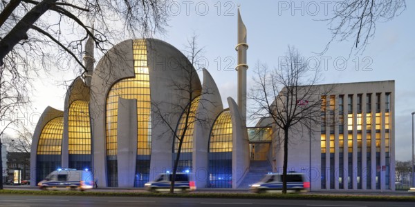 Several police vehicles with flashing lights drive past the Kölne Mosque in Ehrenfeld