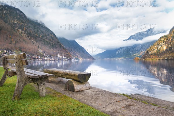 Travel destinations theme image with the Dachstein Mountains reflected in the water of the Hallstatter lake and wooden benches on its shore, in Hallstatt, Austria, Europe