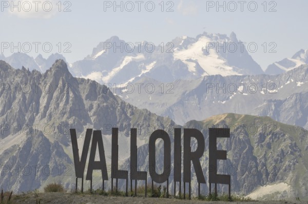 Name of Valloire write in metal letters, Valloire sign against a backdrop of majestic mountains and a clear blue sky