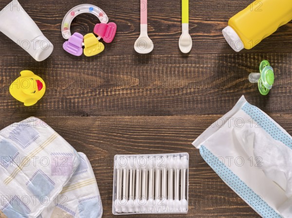 Japanese diapers, wet wipes, baby powder, cream, tither, cotton buds, spoons, soother and duckling on dark brown wooden background with copy space. Flat lay or top view