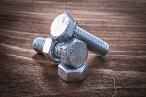 Couple of threaded metal bolts and screw nuts on vintage wooden board repairing concept