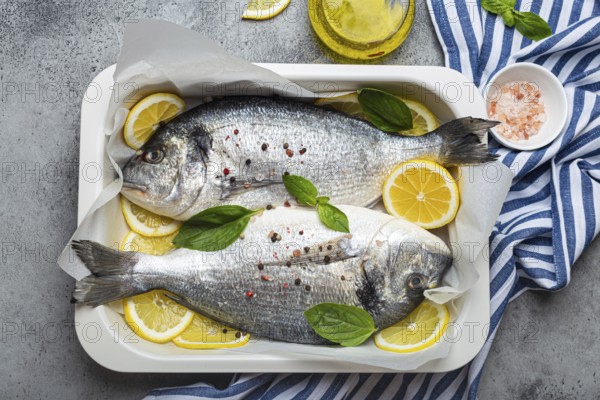 Raw fish dorado in casserole dish with ingredients lemon, fresh basil, bottle of olive oil on wooden cutting board with knife on rustic stone background top view, cooking healthy fish dorado concept, food photography, food photography