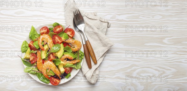 Healthy salad with grilled shrimps, avocado, cherry tomatoes and green leaves on white plate with cutlery on white wooden rustic background top view. Clean eating, nutrition and dieting, copy space, food photography, food photography
