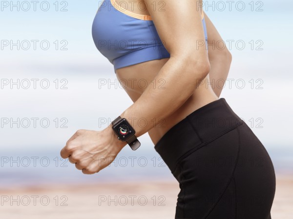 Woman jogging outdoors at the beach with Apple Watch smartwatch on her wrist displaying daily activity and exercise