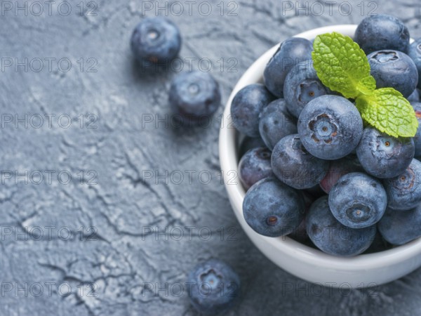 Freshly picked blueberries closeup. Ripe and juicy fresh blueberry with green mint leaves on textured concrete background. Bilberry on gray background with copyspace. Top view or flat lay