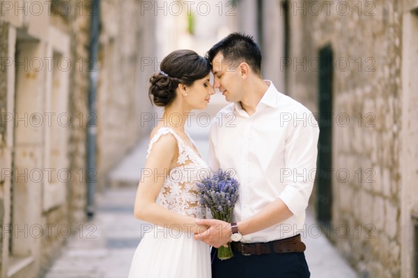 Sibenik, Croatia - 05.06.17: Groom leaned his forehead against the bride's forehead with a lavender bouquet in a white dress against the background of an old city street