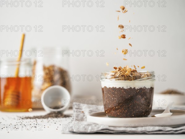 Healthy breakfast concept and idea- chia pudding with organic raw cocoa, white vegan soft cheese and oatmeal granola.Glass jar with chocolate chia pudding with falling oatmeal on white table.Copy space