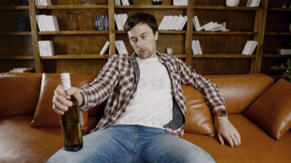 Alcohol addiction at young age. Caucasian male cannot stop drinking alcohol, drunken lonely male drinks wine from bottle. Loneliness, depression and alcoholism during Christmas and New Year holidays