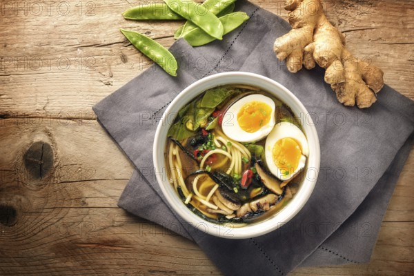 Miso soup with noodles, nori seaweed, snow peas, ginger and an egg in a bowl on a rustic wooden table, top view from above, copy space, selected focus