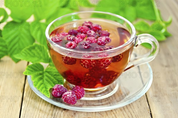 Tea with raspberries in a glass cup, green raspberry leaves on the background of wooden boards