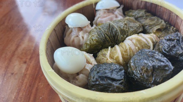 A bamboo steamer filled with diverse dim sum including Japanese siomai, steamed cabbage rolls, and quail eggs on a wooden table