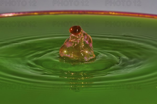 A reddish-brown drop hits green liquid and forms water rings, water droplets, collision, high-speed photography, concept