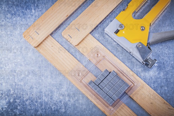 Collection of stapler gun metal staples wooden building board on metallic background