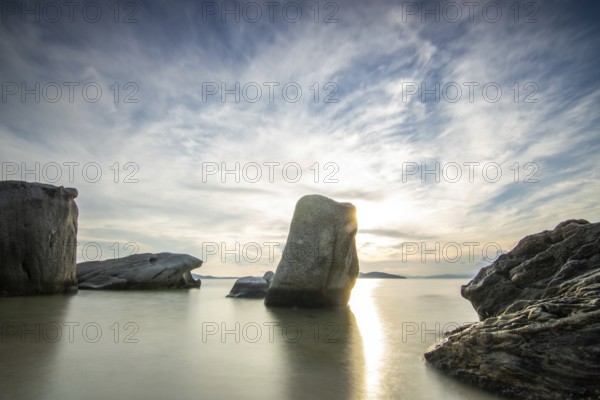 View through rocks on a sandy beach into the sunset. Landscape shot with view to the horizon over the wide sea at the coast of Ouranoupoli, Thessaloniki, Central Macedonia, Greece, Europe