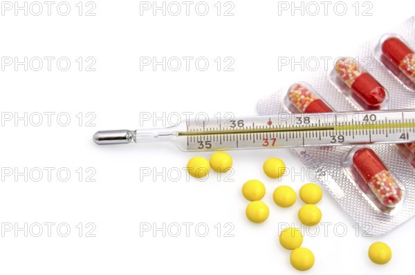 Thermometer with the yellow pills in bulk and red-white capsules in a package on a white background, Russia, Europe