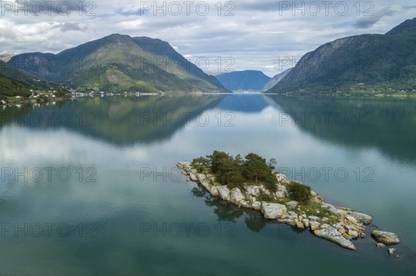 A tranquil lake with a small island surrounded by majestic mountains, their reflections captured in calm waters under a cloudy sky