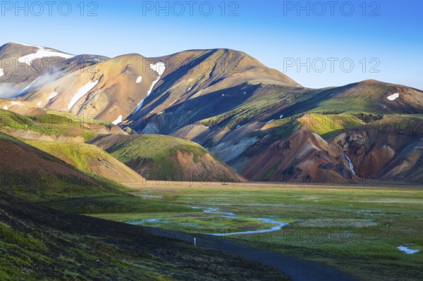 Snow lies in the hollows of colorful rhyolite mountains. Green Valley is flooded with melt water. Early summer morning in the National Park Landmannalaugar, Iceland, Europe