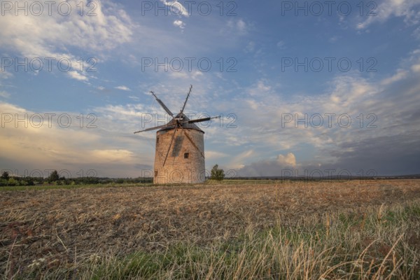 Windmill with wooden sails in a landscape with fields. Meadows and flowers appear in the sunset. Landscape shot in nature with a windmill. Historically atypical for the Balaton region in Hungary