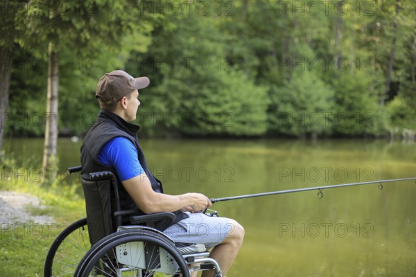 Happy and young disabled or handicapped man fishing at a lake in nature. Popular sport for paraplegics