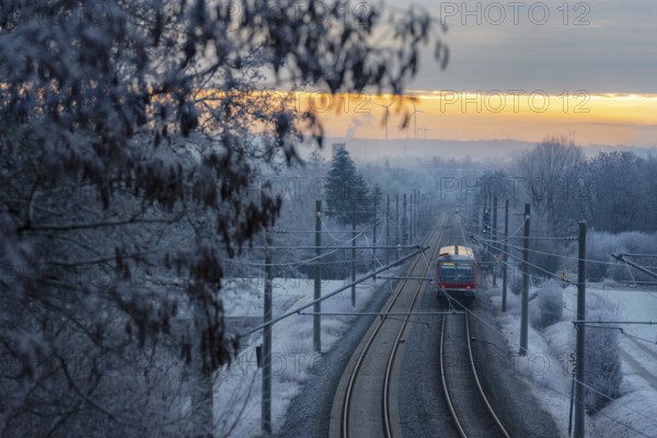 Passenger train traveling on railway tracks through frozen trees, at sunrise, in the German countryside. Winter travel. Public transportation