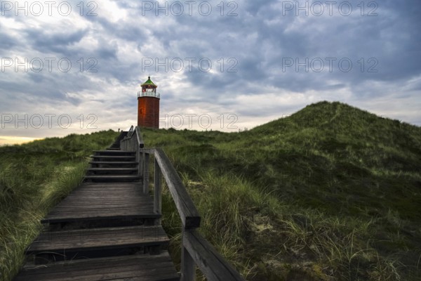 Evening landscape with wooden stairs over marram grass hill, toward red lighthouse, on Sylt island, Germany, Europe