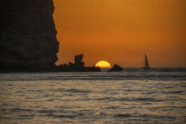 Sunrise during a sandstorm, Calima. The haze-covered horizon turns orange as the sun rises as a ball. A boat is anchored in the sea. Landscape photograph in Gran Tarajal, Canary Islands, Spain, Europe