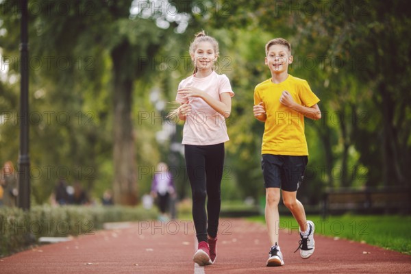 Sports and fitness in adolescence. Caucasian twins boy and girl run on the jogging track in the city park. Two children brother and sister for 10 years running on a rubberised outdoor treadmill