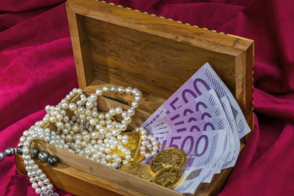 Gold in coins and bars with jewellery on red velvet. Symbolic photo for wealth, luxury, wealth tax. Austria