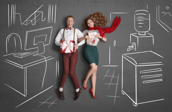 Happy valentines love story concept of an office romance. Young couple at work smiling at each other and exchanging gifts against chalk drawings background