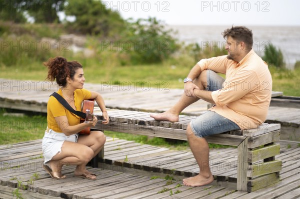 Women squatting playing guitar for her boyfriend in a park near the sea