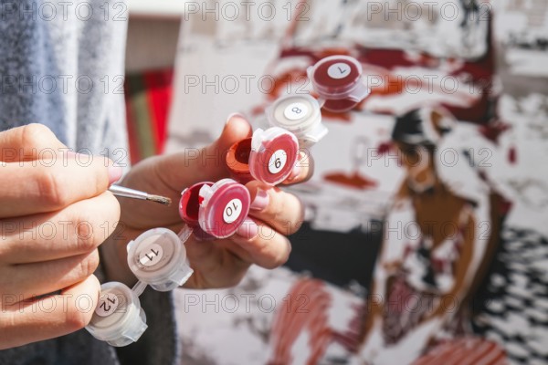 Female hands coloring canvas Picture by numbers car and girl. Creative hobby. Painting for beginners. Leisure activity for stay home isolation, anti-stress idea. Meditation, relax concept Art education. The artist paints with a brush