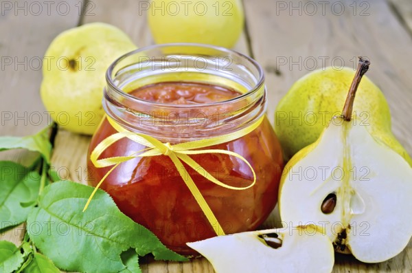 Pear jam in a glass jar, fresh pears, twigs with leaves on a wooden board