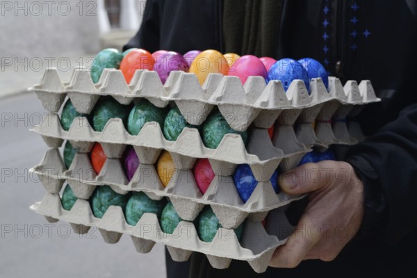 Person holding several stacks of coloured eggs for Easter