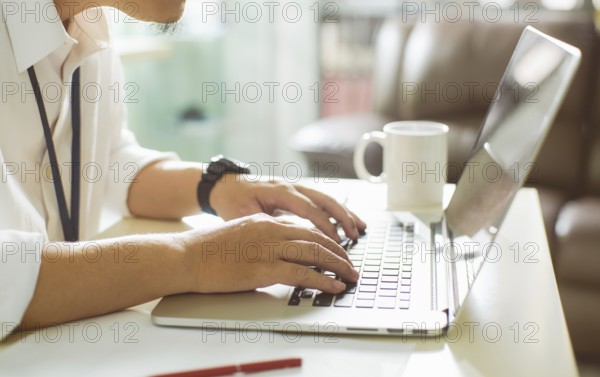 Businessman using laptop with tablet and pen on white table in office with a cup of coffee, side view and selected focus