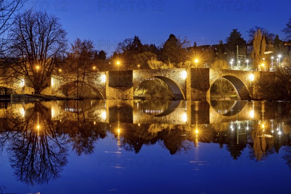 Night scene with illuminated stone bridge and reflecting water, The historic Bartenwetz stone bridge in Melsungen