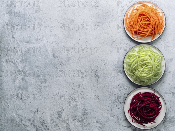 Vegetable noodles - zucchini, carrot, and beetroot noodles on plate over gray cement background. Clean eating, raw vegetarian, food concept. Copy space for text. Top view or flat lay