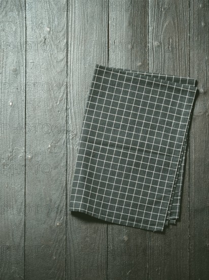 Dark wooden table with balck and white dark linen kitchen towel or textile napkin flat lay. Dark tablecloth on brown gray wood tabletop. Copy space for text. Can use as mock up for design. Vertical