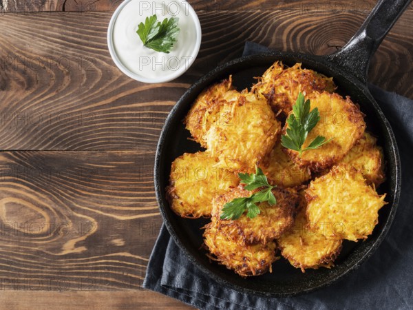 Potatoes pancakes latkes, flapjacks, hash brown or potato vada with white greek yoghurt or sour cream on brown wooden table. Copy space for text