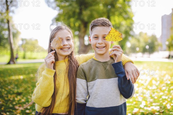 Friendship between siblings. Siblings together outside with bright coloured background. Kids autumn portrait. Brother and sister playing in autumn park leaves. Family active fall weekend concept