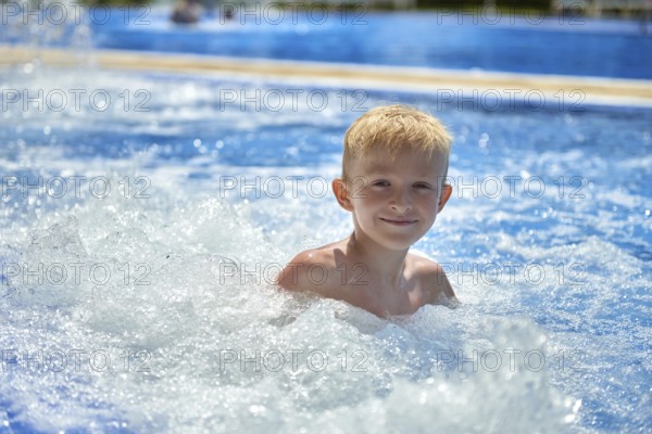 Young boy kid child eight years old splashing in swimming pool having fun leisure activity. Boy happy swimming in a pool. Activities on the pool, children swimming and playing in water, happiness and summertime